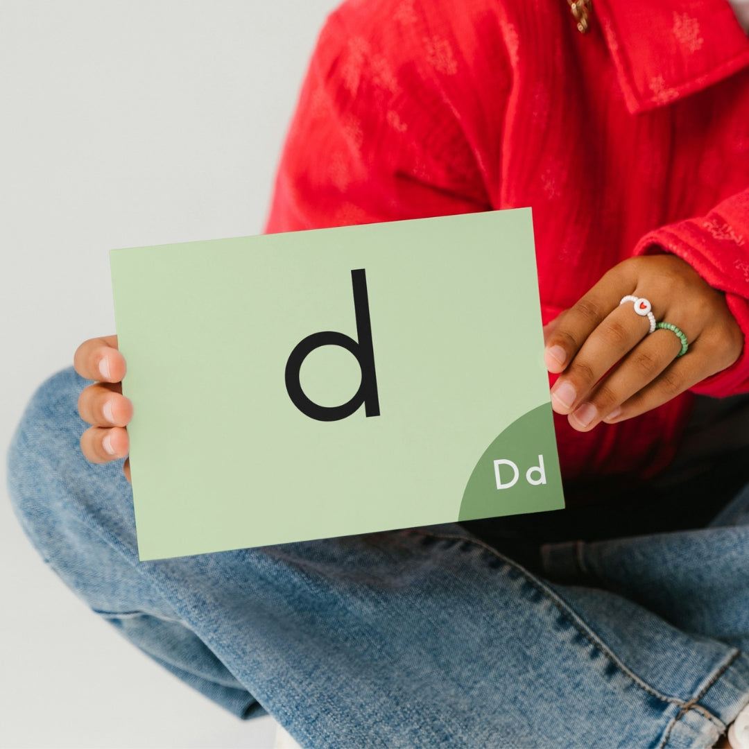 Person holding a card with the letter 'd' on it, wearing a red shirt and blue jeans.