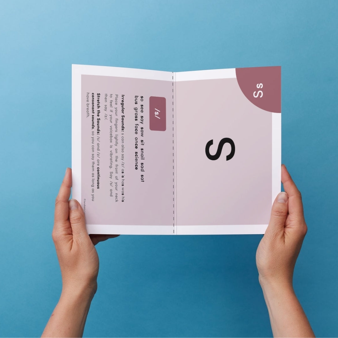 A sheet of paper with an alphabet flashcard printed on it being held up by two hands against a blue background